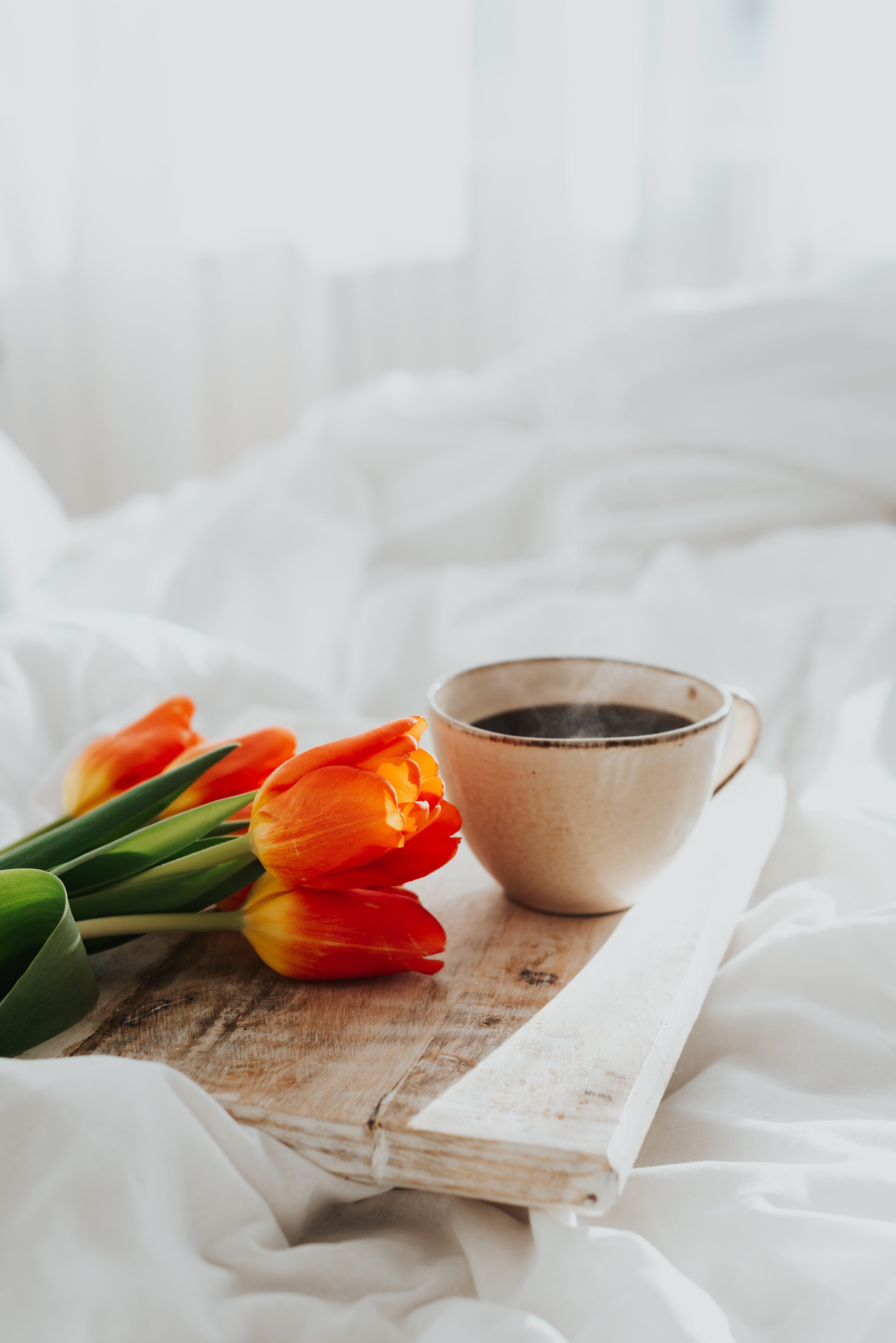 Tray with mug of coffee and bunch of tulips on bed