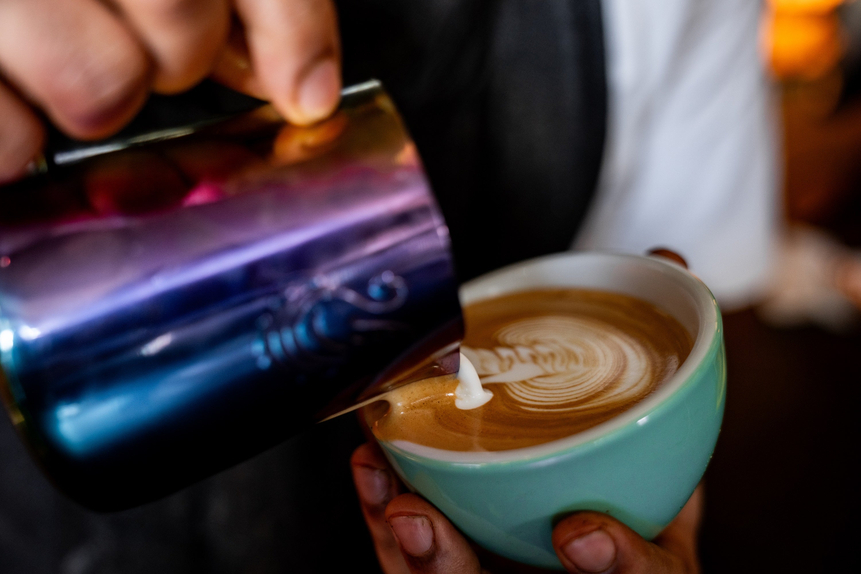 A milk jug being poured into a ceramic mugh with latte art